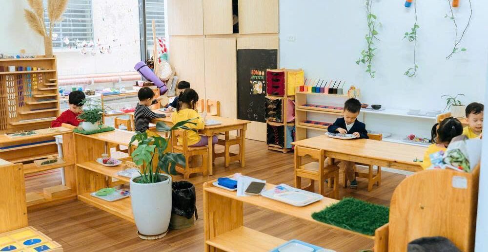 Các bé đọc truyện, sách ở góc thư viện được trang trí bởi cây và bình có lau