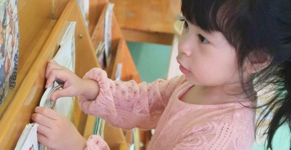 Bé chọn sách trên kệ sách